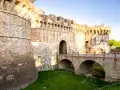 Antiche mura di Colle Val d'Elsa con un ponte ad arco che conduce a un portone fortificato.