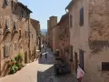 Un vicolo medievale a Certaldo, cosa vedere: case in mattoni, finestre con persiane, fiori e un uomo con mascherina.