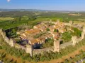 Borgo medievale fortificato nella valle del Chianti, con torri e mura antiche immerse nel verde della campagna toscana.