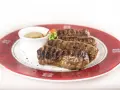 Mici grigliati su un piatto rosso, un classico per sapere cosa mangiare a Bucarest. Serviti con salsa.