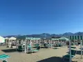Spiaggia attrezzata a Marina di Pietrasanta con lettini e ombrelloni a righe verdi e bianche, sullo sfondo le montagne.