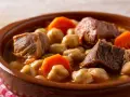 Un saporito cocido madrileño, uno dei piatti tipici di Madrid, con ceci, carne e carote in una ciotola di terracotta.
