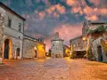 Piazza medievale illuminata al tramonto, con edifici in pietra e un campanile. Un luogo incantevole dove scoprire cosa vedere.