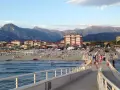 Passeggiata sul molo di Camaiore, dove si trova una spiaggia attrezzata con ombrelloni e montagne sullo sfondo.