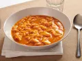 Piatto tipico pisano: trippa alla pisana in un bianco piatto, servita con forchetta e cucchiaio.