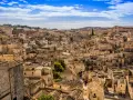 Panoramica di Matera, la città più antica del mondo, con i suoi Sassi scavati nella roccia e le case in pietra sotto un cielo azzurro.