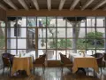 Tavoli apparecchiati in un elegante ristorante stellato Veneto, con vista su un cortile interno con alberi e piante in vaso.
