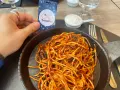 A hand holds a Travel365 tag over a plate of spaghetti with red sauce.