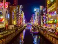 Un canale illuminato da insegne al neon a Osaka, cosa vedere: un tour in battello tra edifici vibranti e riflessi sull'acqua.
