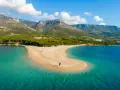 La Croazia offre il mare più bello: una spiaggia dorata a forma di lingua si protende in acque cristalline, con montagne verdi sullo sfondo.