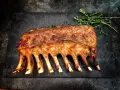 Carré d'agnello arrosto, uno dei 5 piatti tipici della Sardegna, guarnito con erbe aromatiche su una pietra scura.
