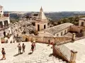 Panoramica di una città barocca in Sicilia orientale, cosa vedere: un borgo arroccato con chiese e case in pietra, turisti che esplorano le scalinate.