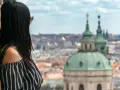 Vista di una donna con capelli scuri appoggiata a un muro di mattoni, con lo sguardo rivolto verso un panorama urbano di **città europee da visitare in 3 giorni**.