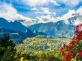 Vista panoramica di un villaggio verdeggiante sull'isola di Reunion, incastonato tra imponenti montagne blu e fiori rossi vibranti.