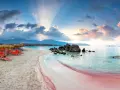 Spiaggia rosa con lettini arancioni e ombrelloni di paglia, mare turchese e montagne sullo sfondo. Un luogo da sogno tra i 10 mari più belli del mondo.
