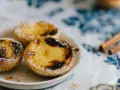 Pastéis de nata, un must per sapere cosa mangiare a Porto. Dolci cremosi su un piatto, spolverati di zucchero a velo, con cannella sullo sfondo.