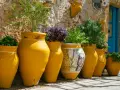 Vasi gialli decorati con un volto femminile, piante rigogliose e un muro in pietra: scorci suggestivi di Bagheria cosa vedere.
