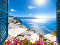 Vista mozzafiato su Santorini, perfetta per sapere dove andare in vacanza a giugno. Case bianche a picco sul mare blu intenso, fiori colorati e sole splendente.