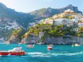 Barche a vela solcano le acque turchesi, con case colorate aggrappate alle scogliere dei paesi della costiera amalfitana.