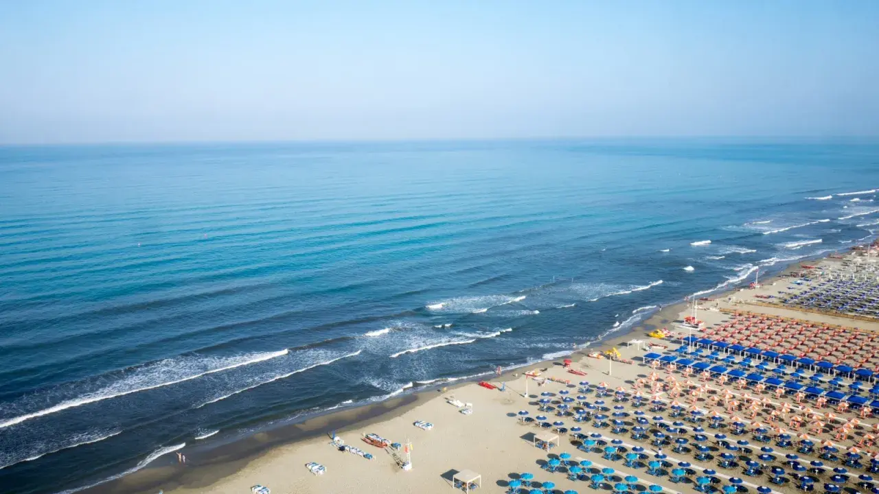 Ampia spiaggia attrezzata al lido di Camaiore, con file ordinate di ombrelloni blu e arancioni che si estendono fino al mare calmo.