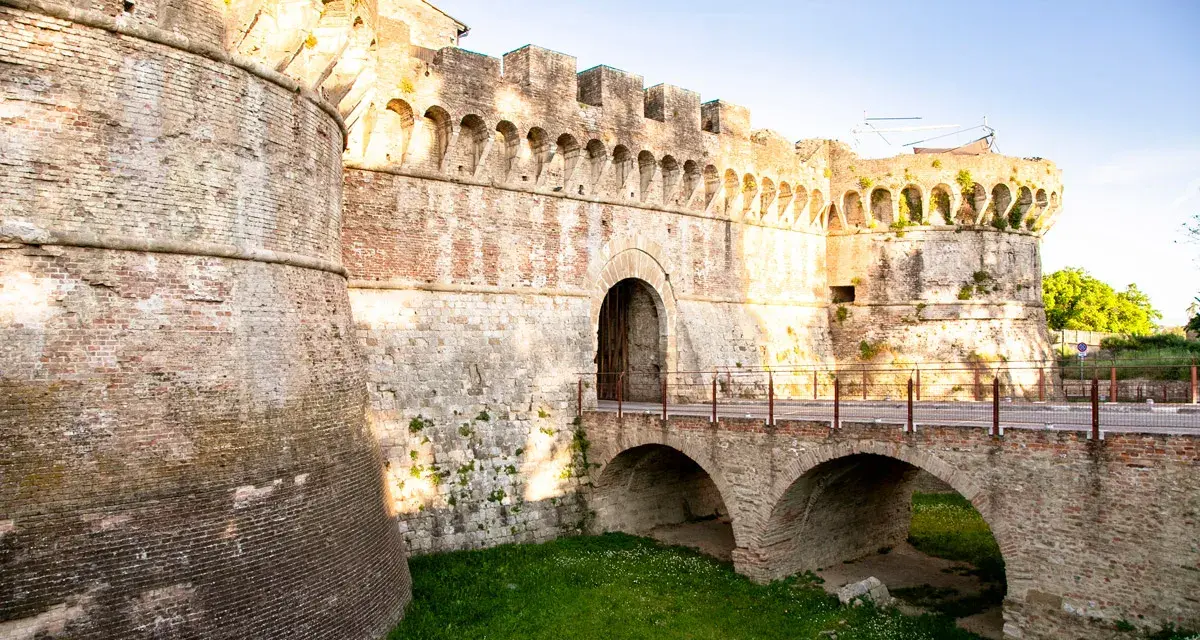 Antiche mura di Colle Val d'Elsa con un ponte ad arco che conduce a un portone fortificato.