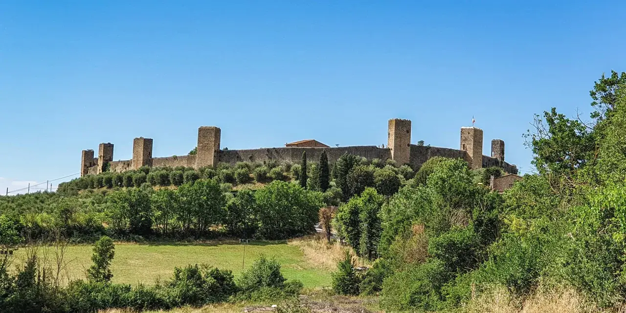 Monteriggioni cosa vedere: imponenti mura medievali con torri quadrate su una collina verdeggiante, sotto un cielo azzurro.