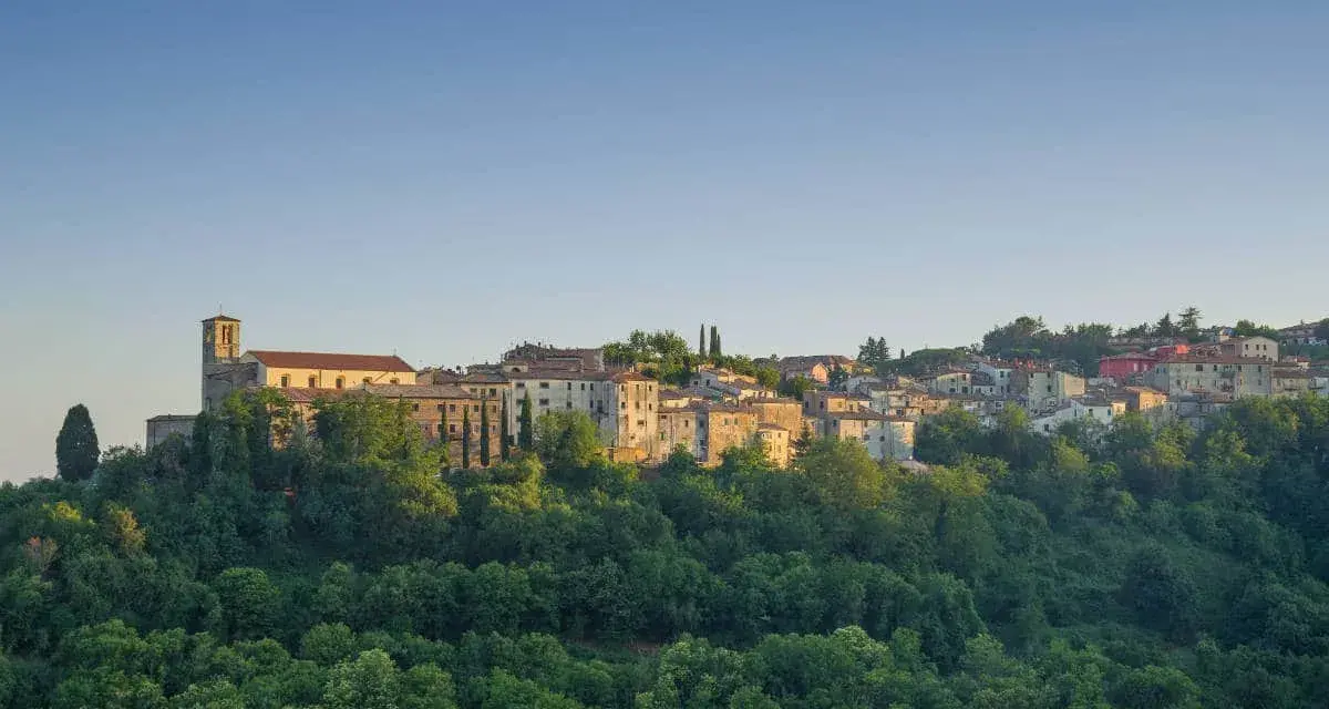 Borgo collinare con chiesa e case in pietra, immerso nel verde. Un luogo incantevole dove scansano cosa vedere, tra storia e natura.