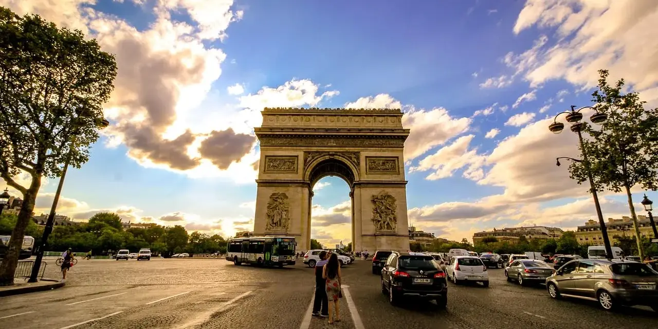 Arco di Trionfo, un'icona di cosa vedere a Parigi, con traffico e nuvole al tramonto.