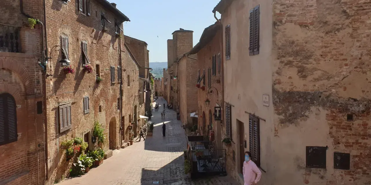 Un vicolo medievale a Certaldo, cosa vedere: case in mattoni, finestre con persiane, fiori e un uomo con mascherina.