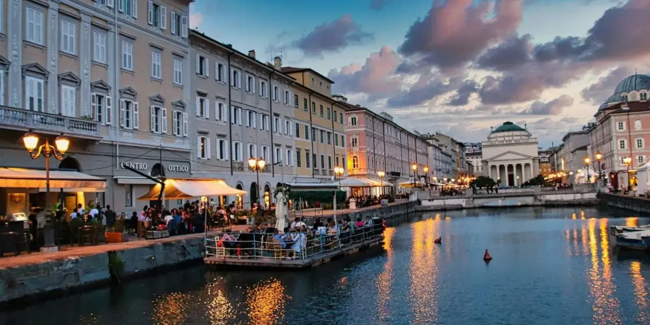 Serata magica a Trieste, uno dei tanti posti belli in Italia. Canale illuminato, palazzi storici e gente ai tavolini all'aperto.