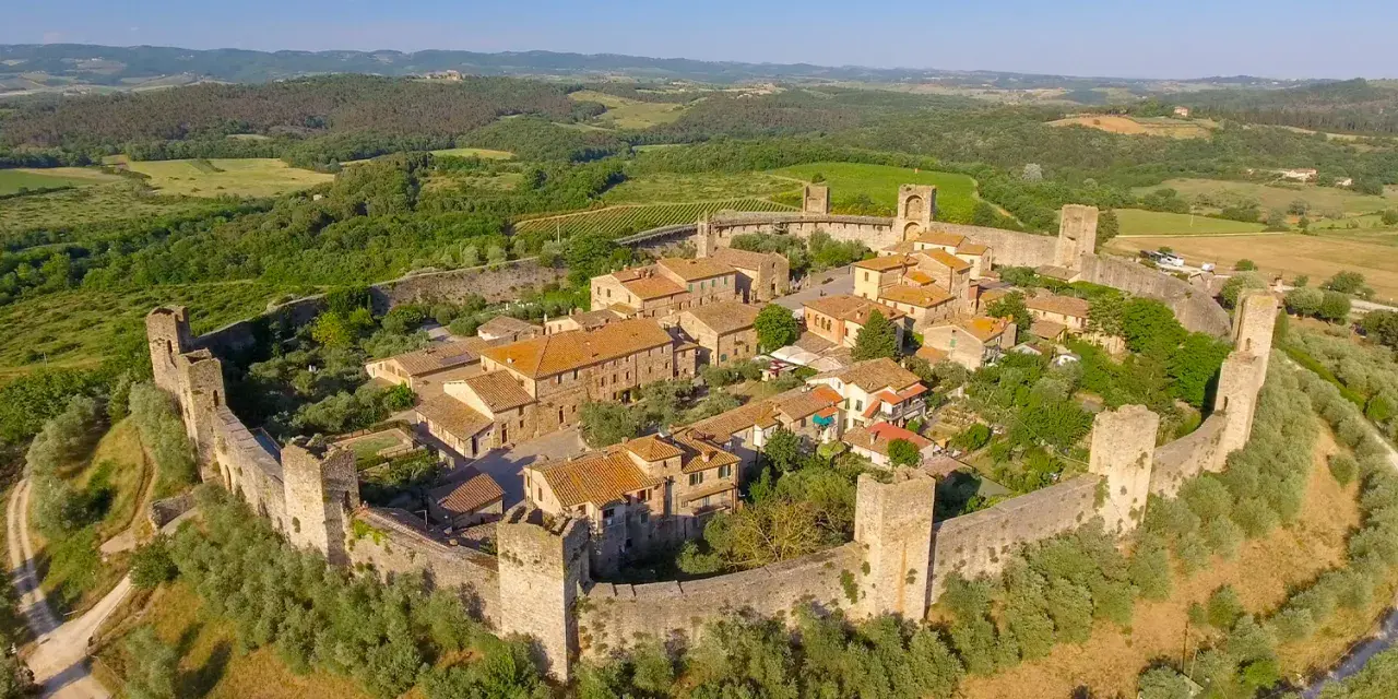 Borgo medievale fortificato nella valle del Chianti, con torri e mura antiche immerse nel verde della campagna toscana.
