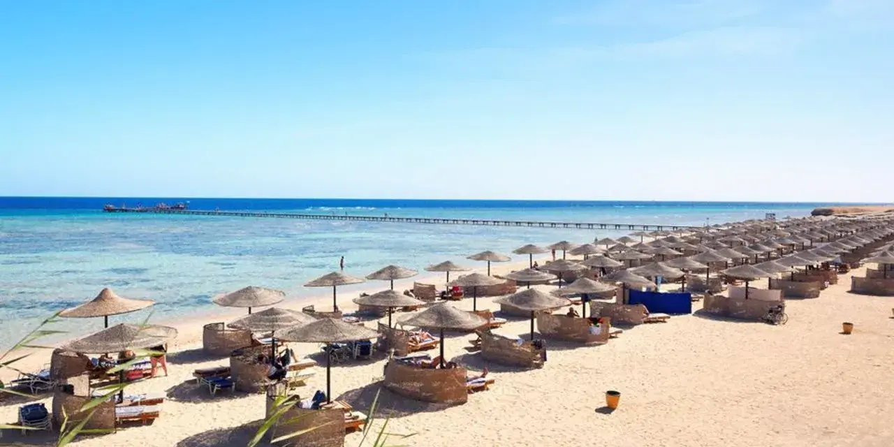 Spiaggia di Marsa Alam con file di ombrelloni e lettini, molo sull'acqua cristallina. Ideale per escursioni e relax.