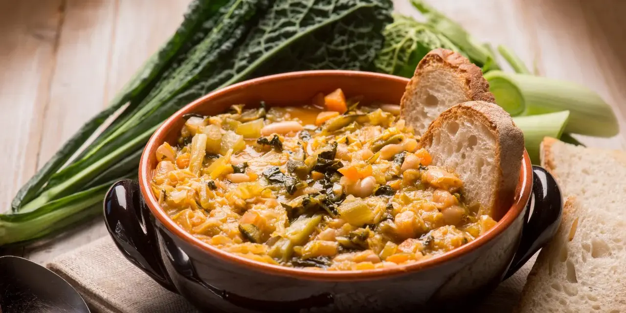 Zuppa di verdure e fagioli, un classico dei cibi tipici toscani, servita con pane rustico e contornata da cavolo nero.