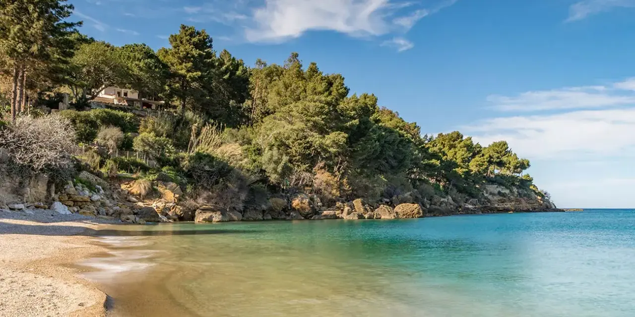 Spiaggia tranquilla con acque cristalline e una villa immersa nel verde sulla costa di Castellammare del Golfo.
