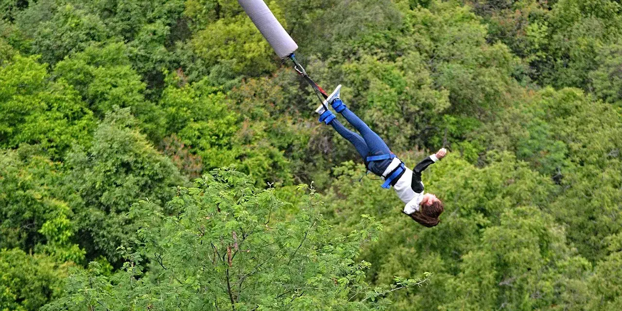 Donna in caduta libera durante un'emozionante esperienza di bungee jumping in Italia, circondata da una lussureggiante foresta verde.