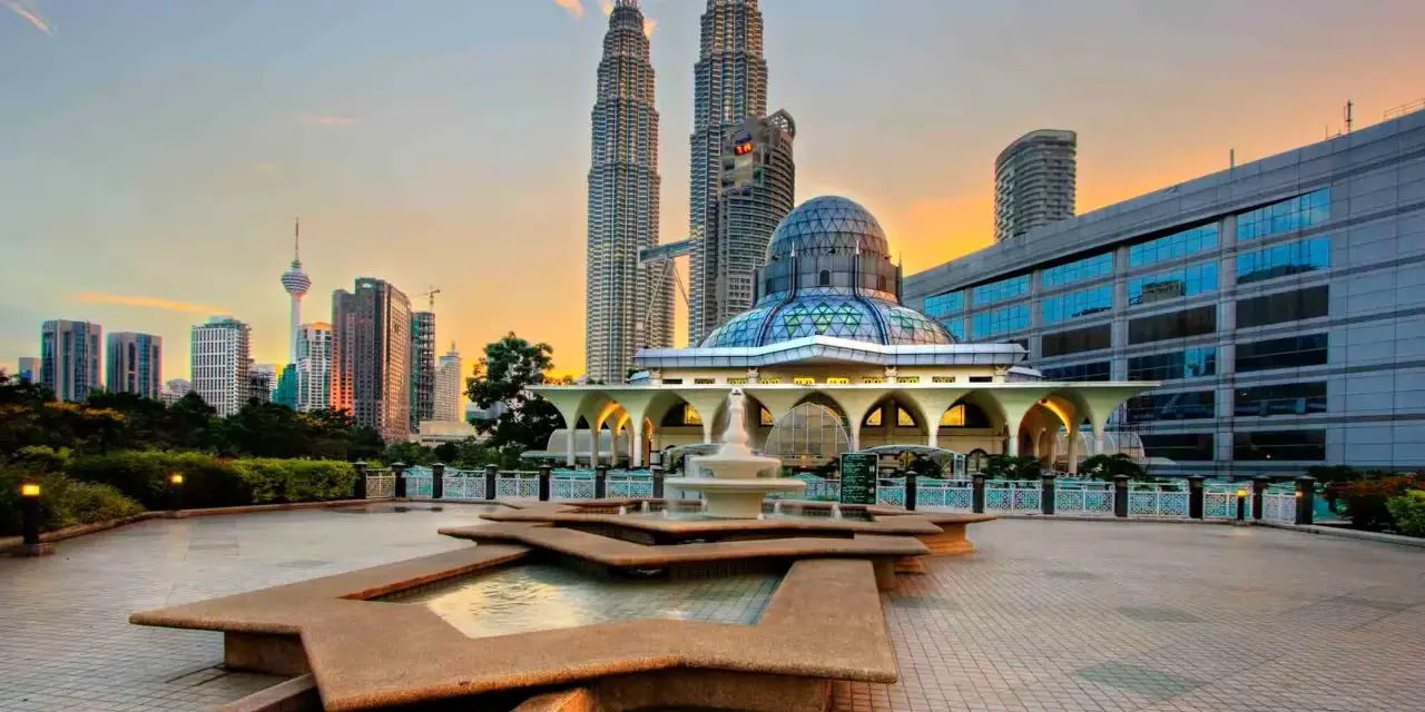 Le Petronas Towers dominano lo skyline di Kuala Lumpur, con una moschea moderna e fontane in primo piano. Un'ottima vista di cosa vedere a Kuala Lumpur al tramonto.