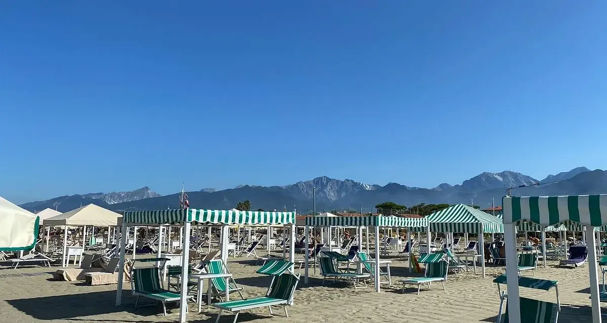 Spiaggia attrezzata a Marina di Pietrasanta con lettini e ombrelloni a righe verdi e bianche, sullo sfondo le montagne.