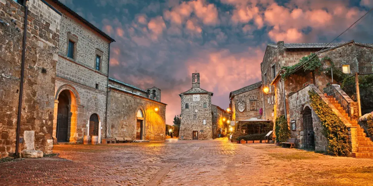 Piazza medievale illuminata al tramonto, con edifici in pietra e un campanile. Un luogo incantevole dove scoprire cosa vedere.