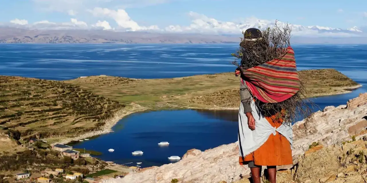 Donna indigena con fascina di legna, vista sul Lago Titicaca, un luogo imperdibile da vedere in Bolivia.