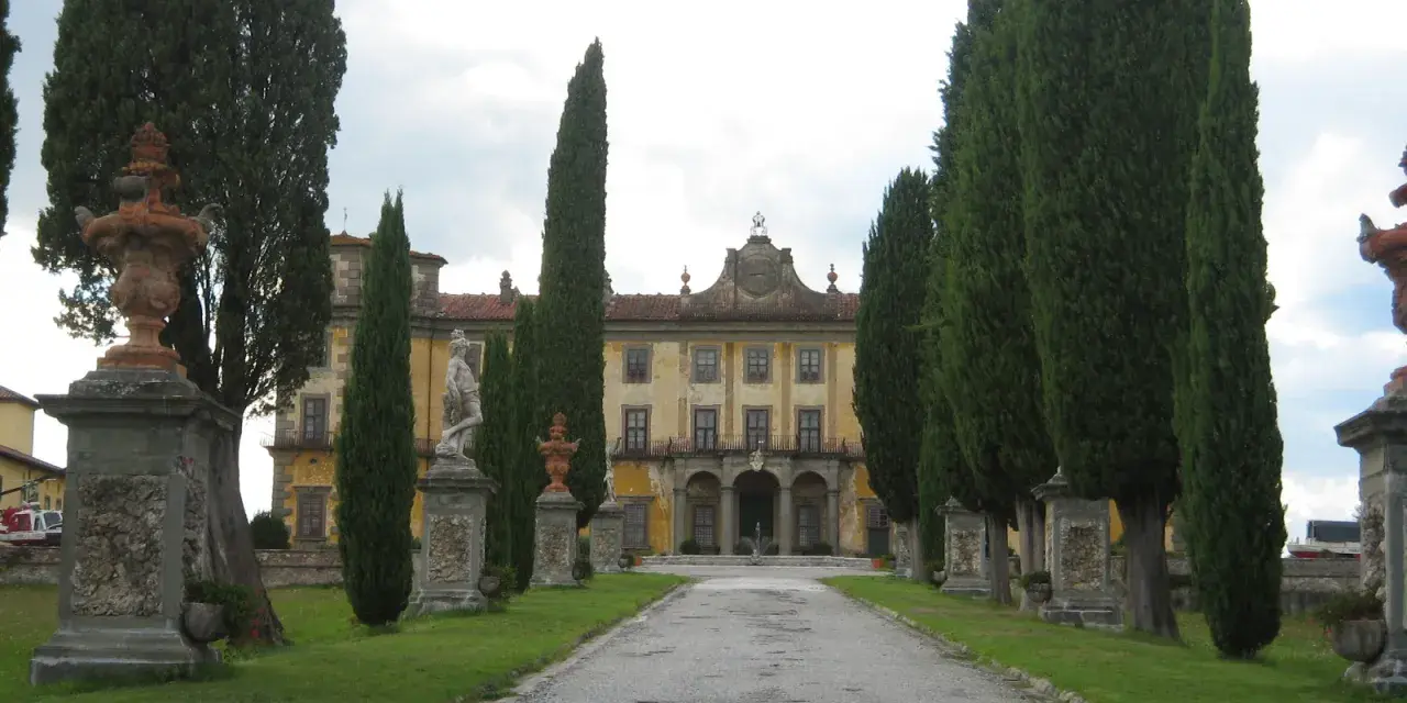 Viale alberato conduce a un palazzo giallo, con statue e fontane, tipico di un borgo a Buggiano.