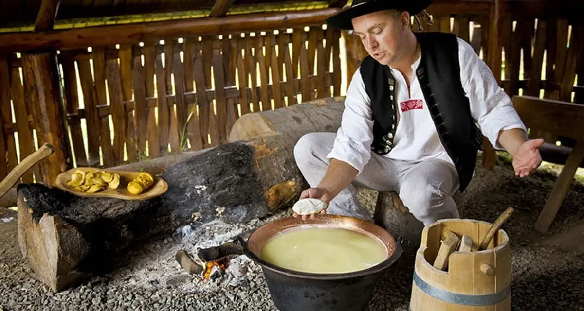 Uomo in abito tradizionale polacco prepara un prodotto tipico della Polonia: formaggio in un paiolo di rame.