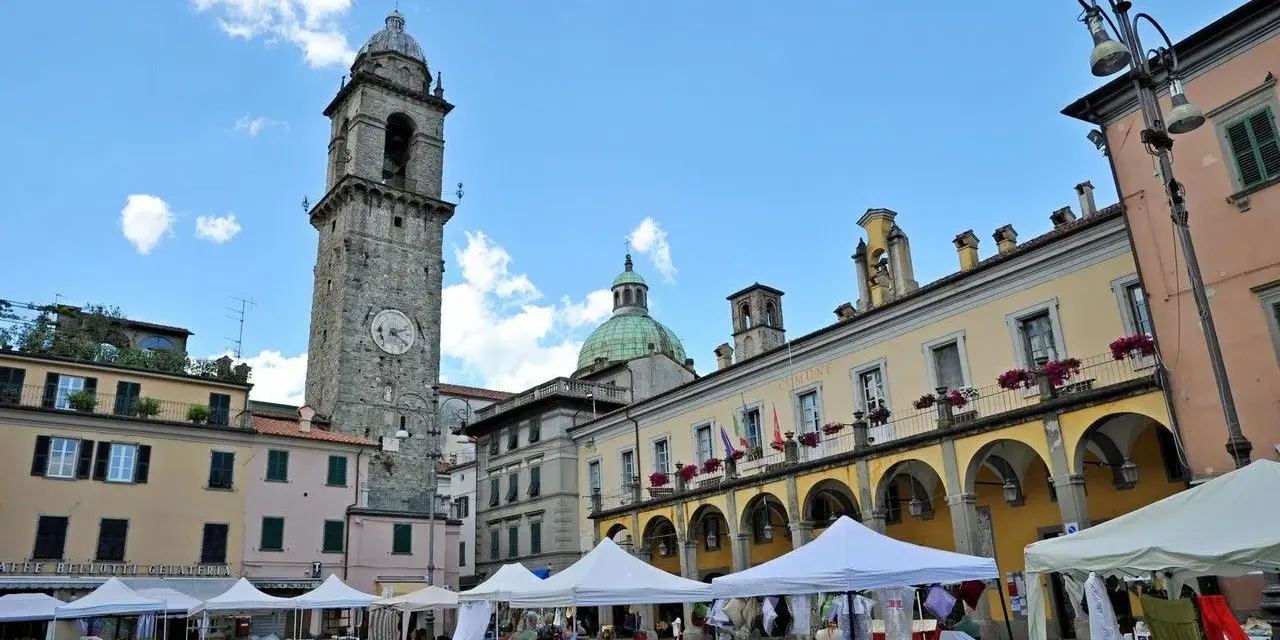 Mercato in piazza a Pontremoli, con la torre civica e il palazzo del Comune. Ecco cosa vedere a Pontremoli: un'atmosfera vivace.