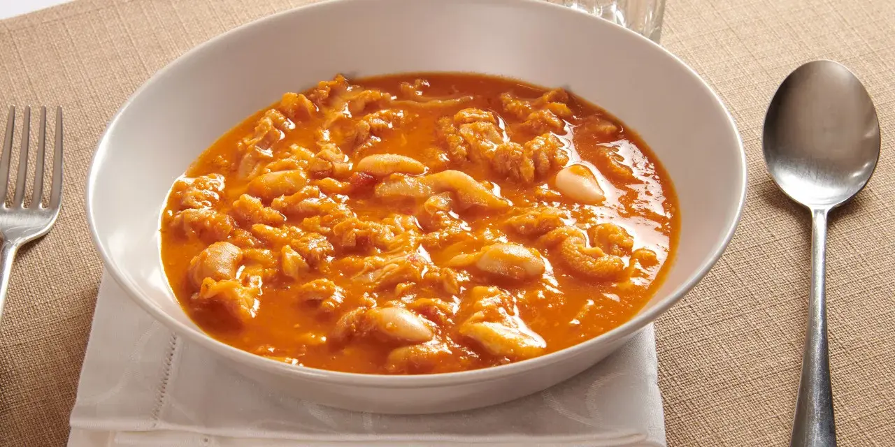 Piatto tipico pisano: trippa alla pisana in un bianco piatto, servita con forchetta e cucchiaio.