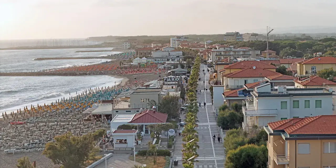 Vista aerea del lungomare di Marina di Cecina con spiaggia attrezzata, mare calmo e case con tetti rossi.