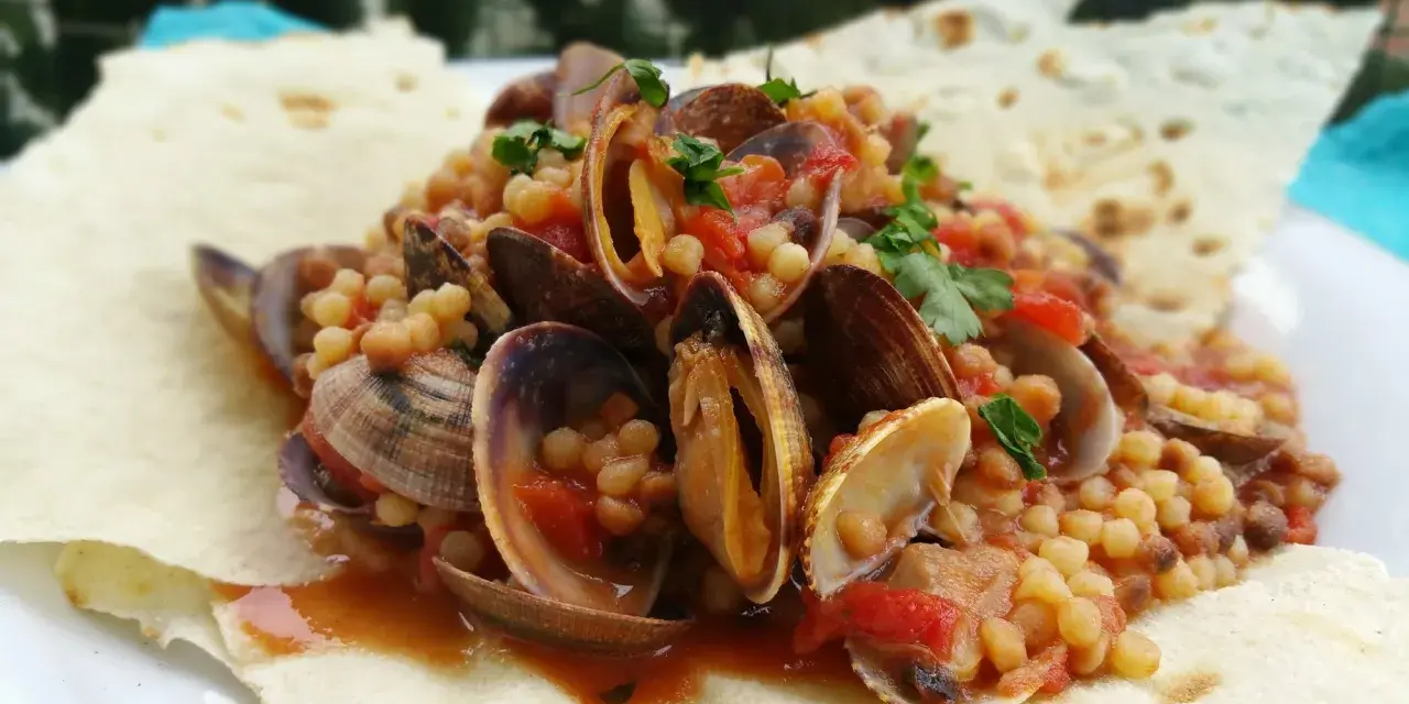 Vongole e fregola, un classico dei piatti tipici sardi, servite su pane carasau croccante.
