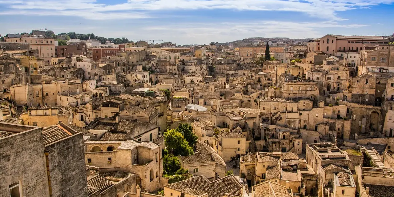 Panoramica di Matera, la città più antica del mondo, con i suoi Sassi scavati nella roccia e le case in pietra sotto un cielo azzurro.