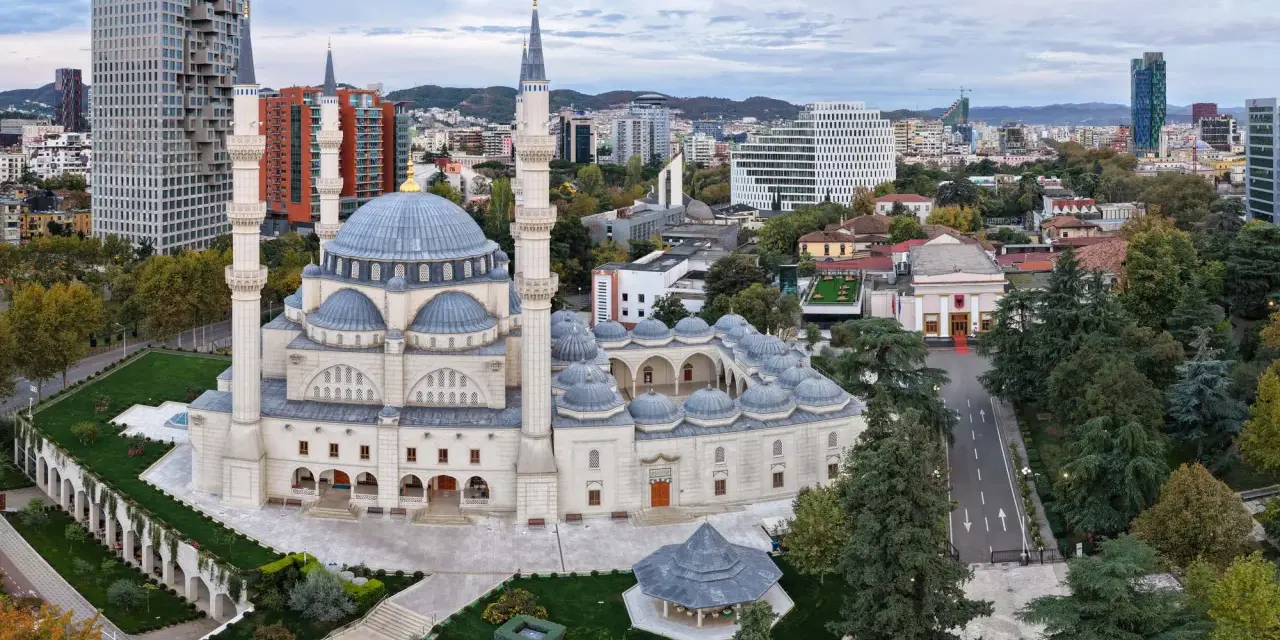 La Grande Moschea e il panorama urbano moderno mostrano dove si trova Tirana, con grattacieli e colline sullo sfondo.