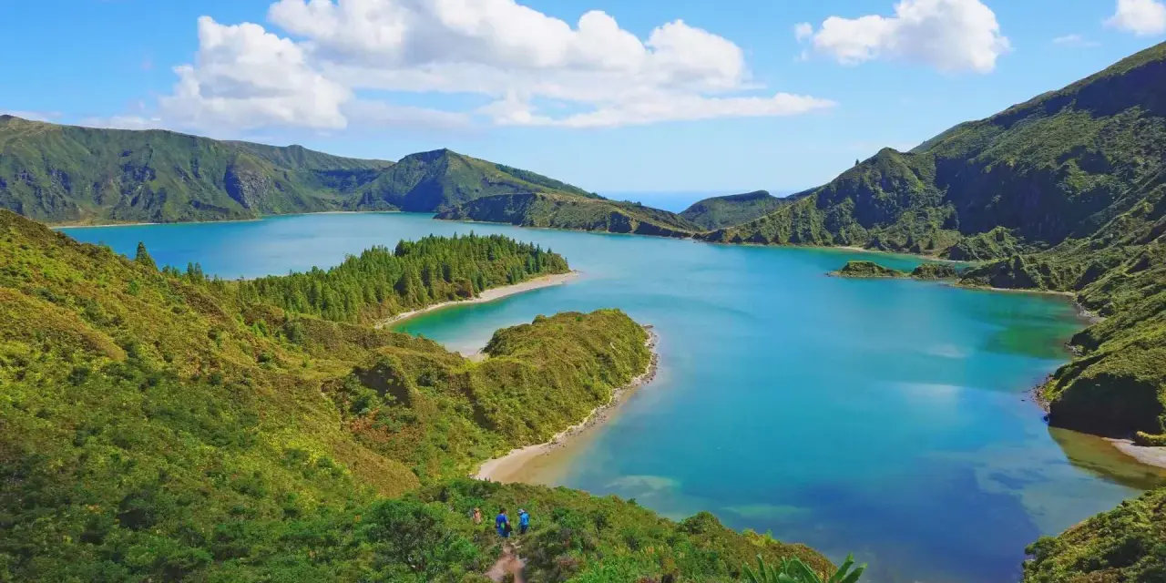 Lago blu circondato da colline verdi lussureggianti, con piccole isole e una spiaggia sabbiosa. Perfetto per capire quando andare alle Azzorre.
