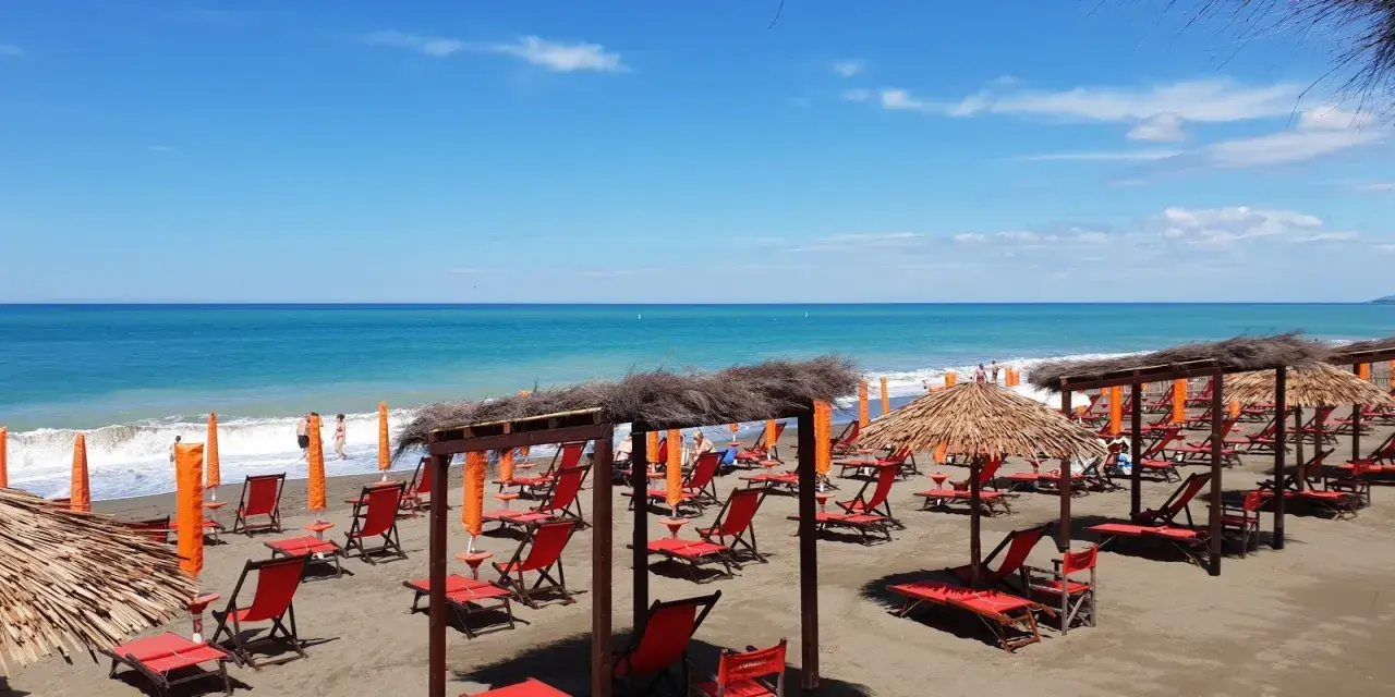 Spiaggia attrezzata a Marina di Bibbona con lettini rossi, ombrelloni di paglia e il mare azzurro sullo sfondo.