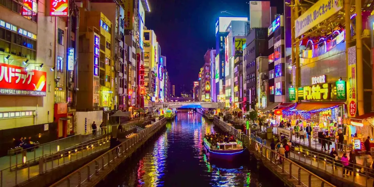 Un canale illuminato da insegne al neon a Osaka, cosa vedere: un tour in battello tra edifici vibranti e riflessi sull'acqua.